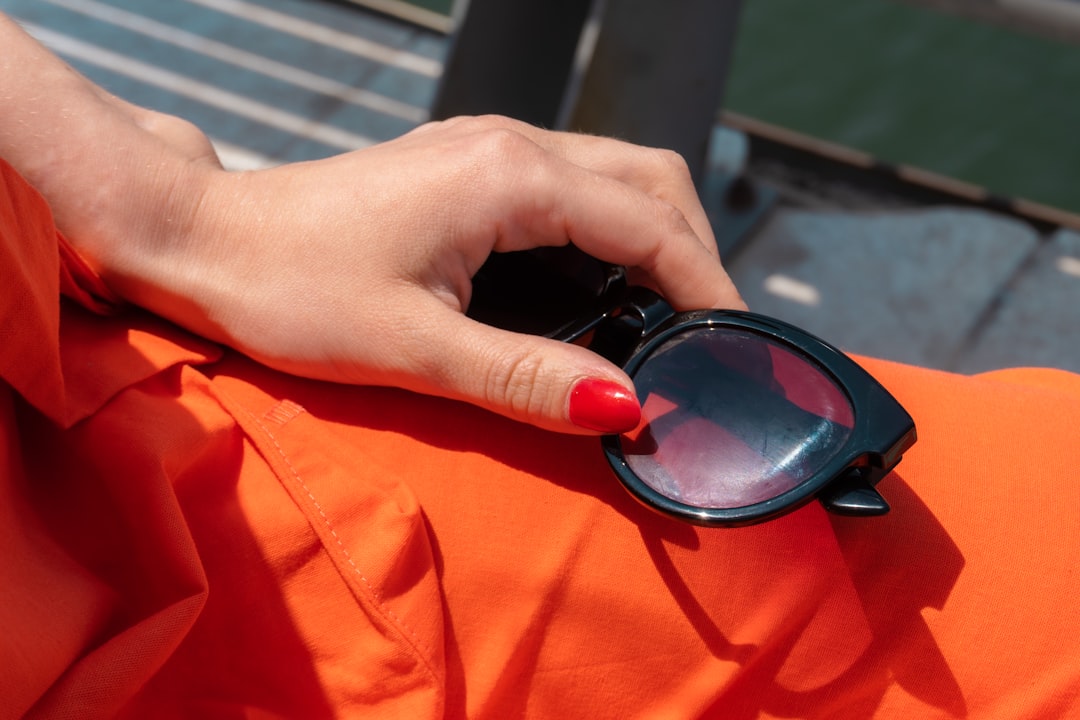 Hand with red nails holding sunglasses on orange fabric